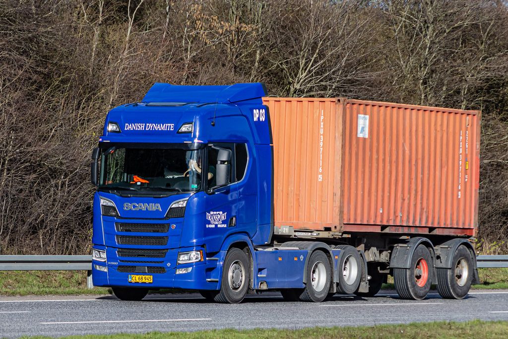 A blue truck hauling an orange container on a motorway