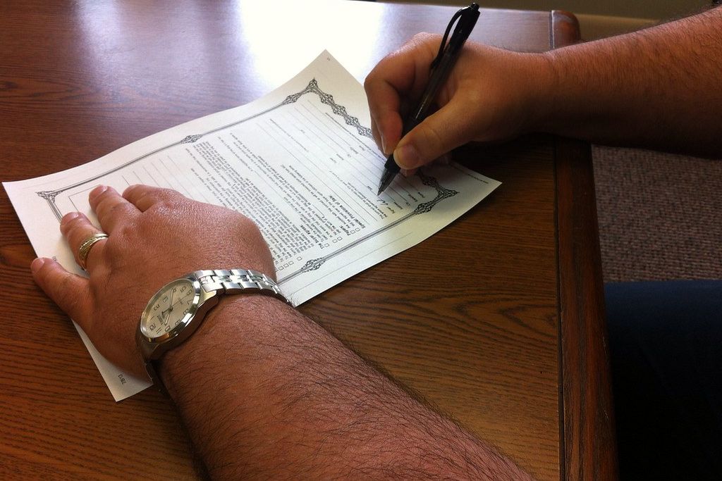 A hand signing a printed form on a desk